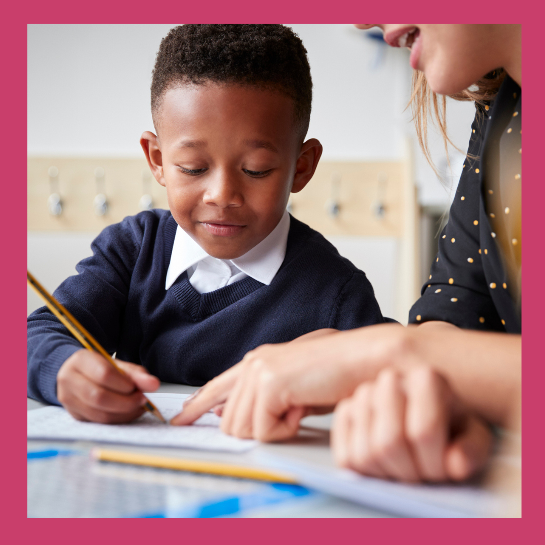 Female primary school teacher helping a young school boy sitting at table in a classroom